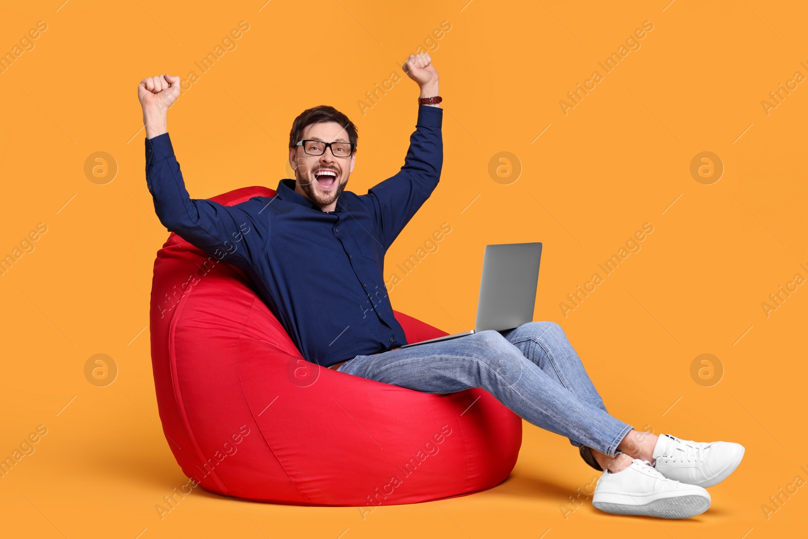 Photo of Emotional man with laptop sitting in beanbag chair against yellow background