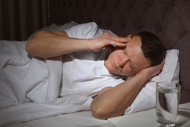 Handsome young man suffering from headache while lying in bed at night