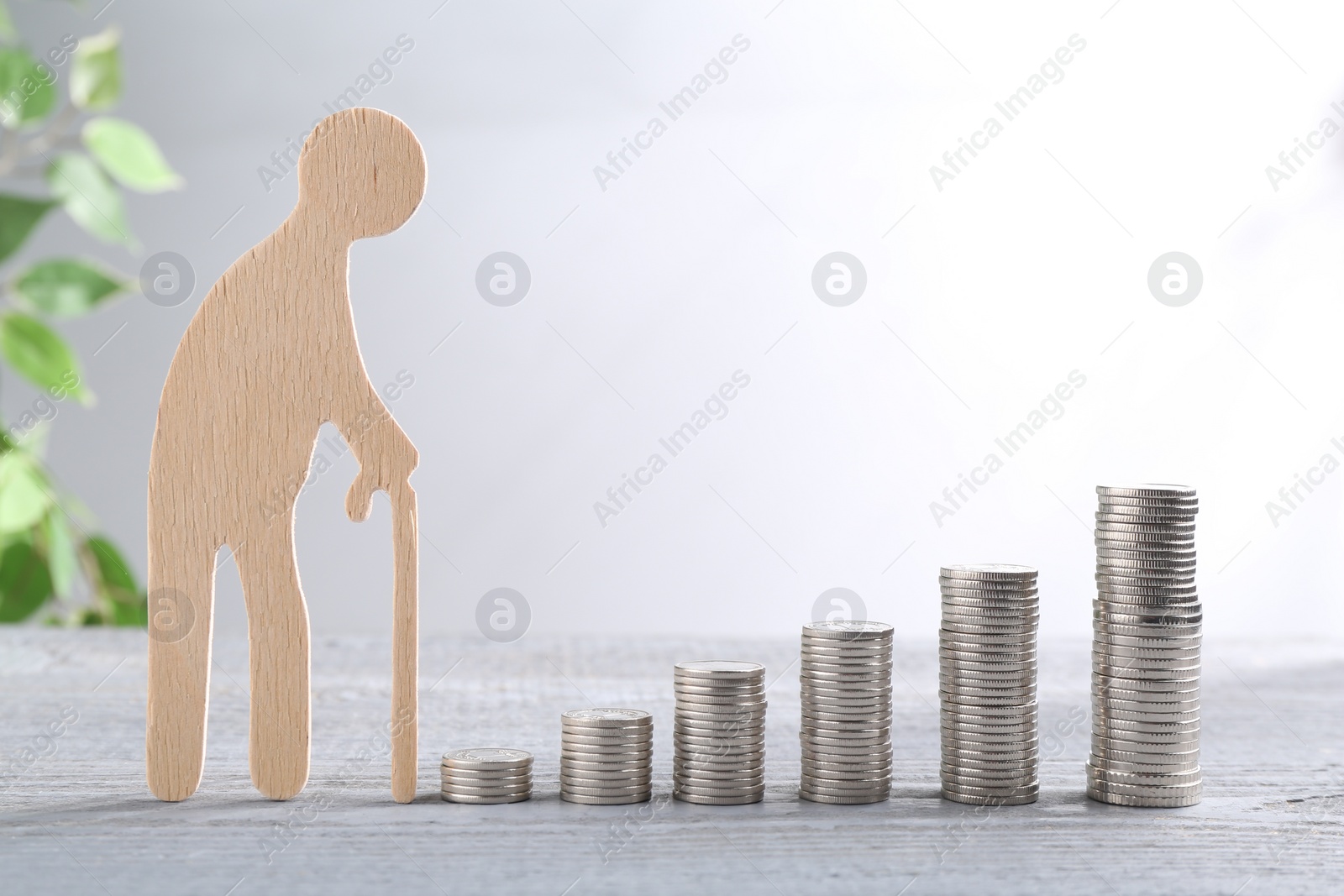 Photo of Pension savings. Figure of senior man and stacked coins on grey wooden table