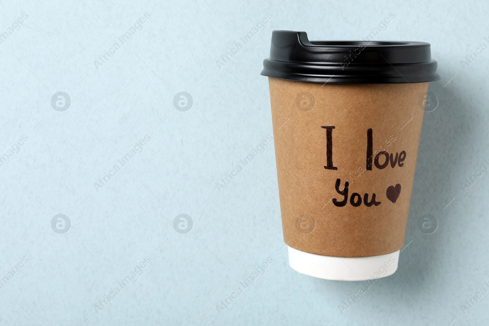 Photo of Paper cup with phrase I Love You on light blue background, top view