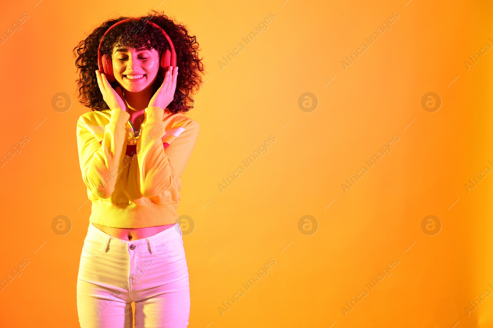 Photo of Beautiful young woman listening to music with headphones on color background in neon lights. Space for text