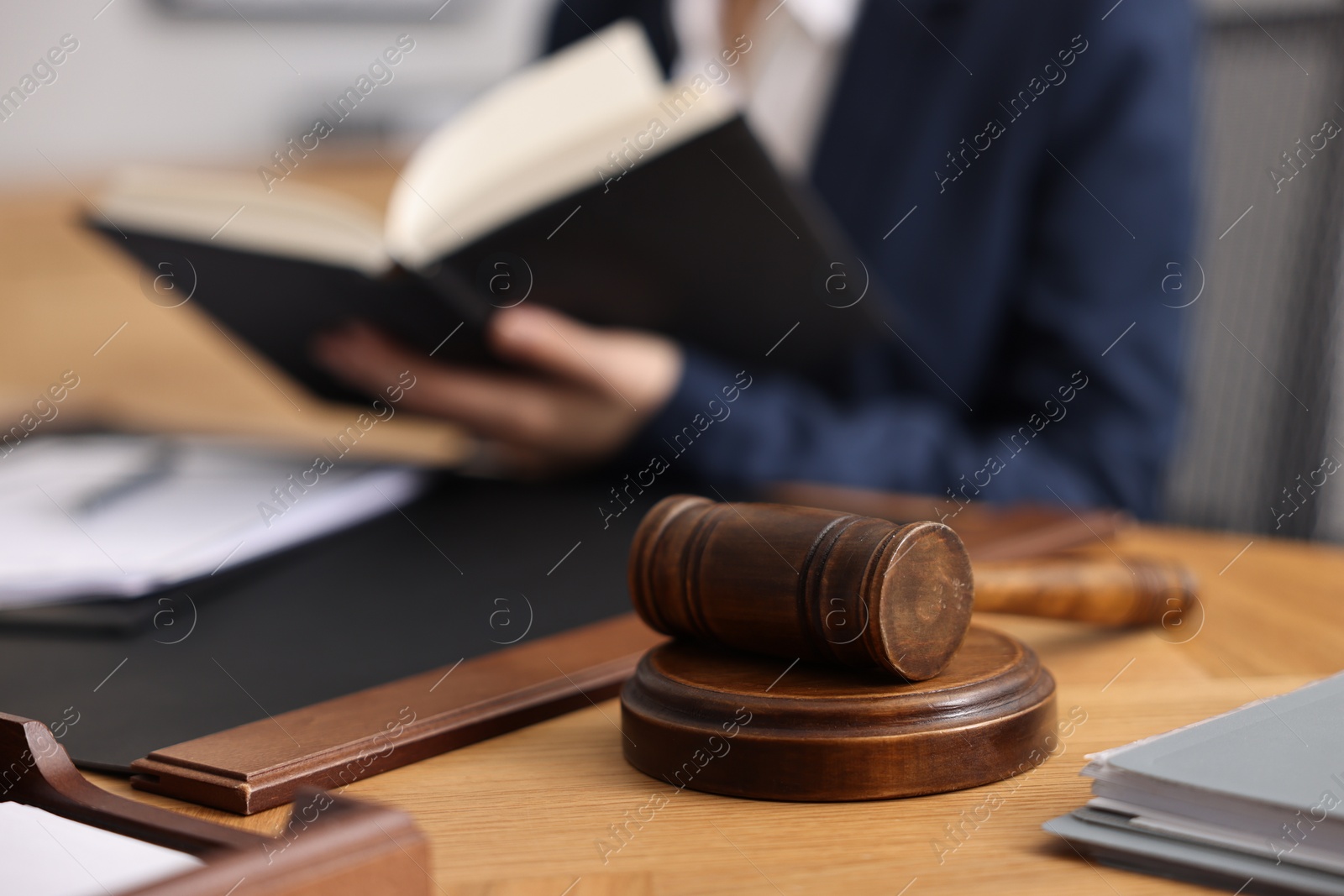 Photo of Notary reading book at wooden table in office, focus on gavel
