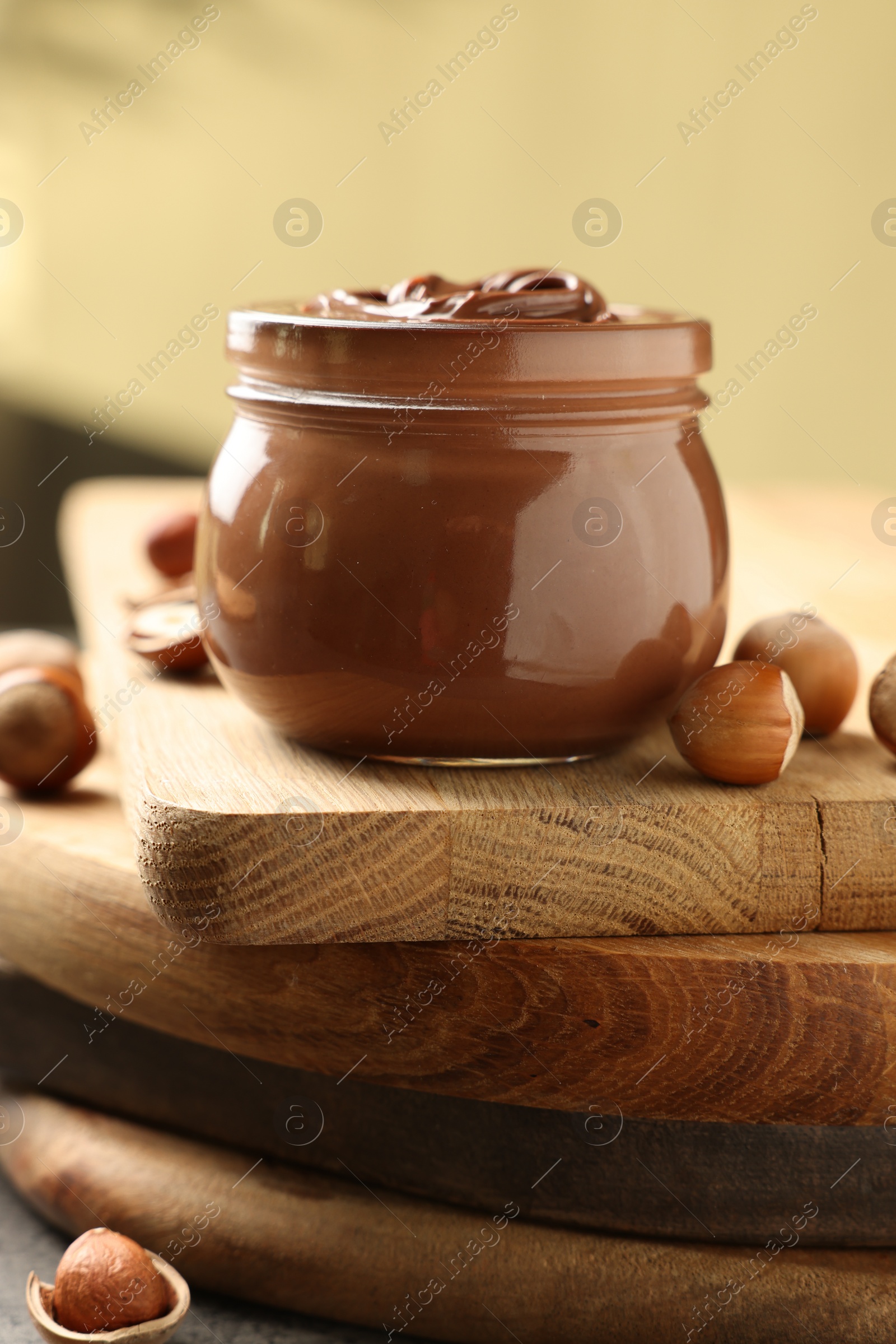 Photo of Glass jar with tasty chocolate hazelnut spread and nuts on wooden board