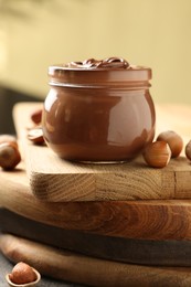 Photo of Glass jar with tasty chocolate hazelnut spread and nuts on wooden board