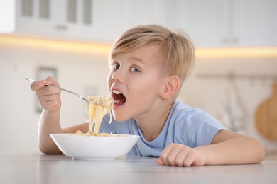 Photo of Boy eating tasty pasta at table in kitchen