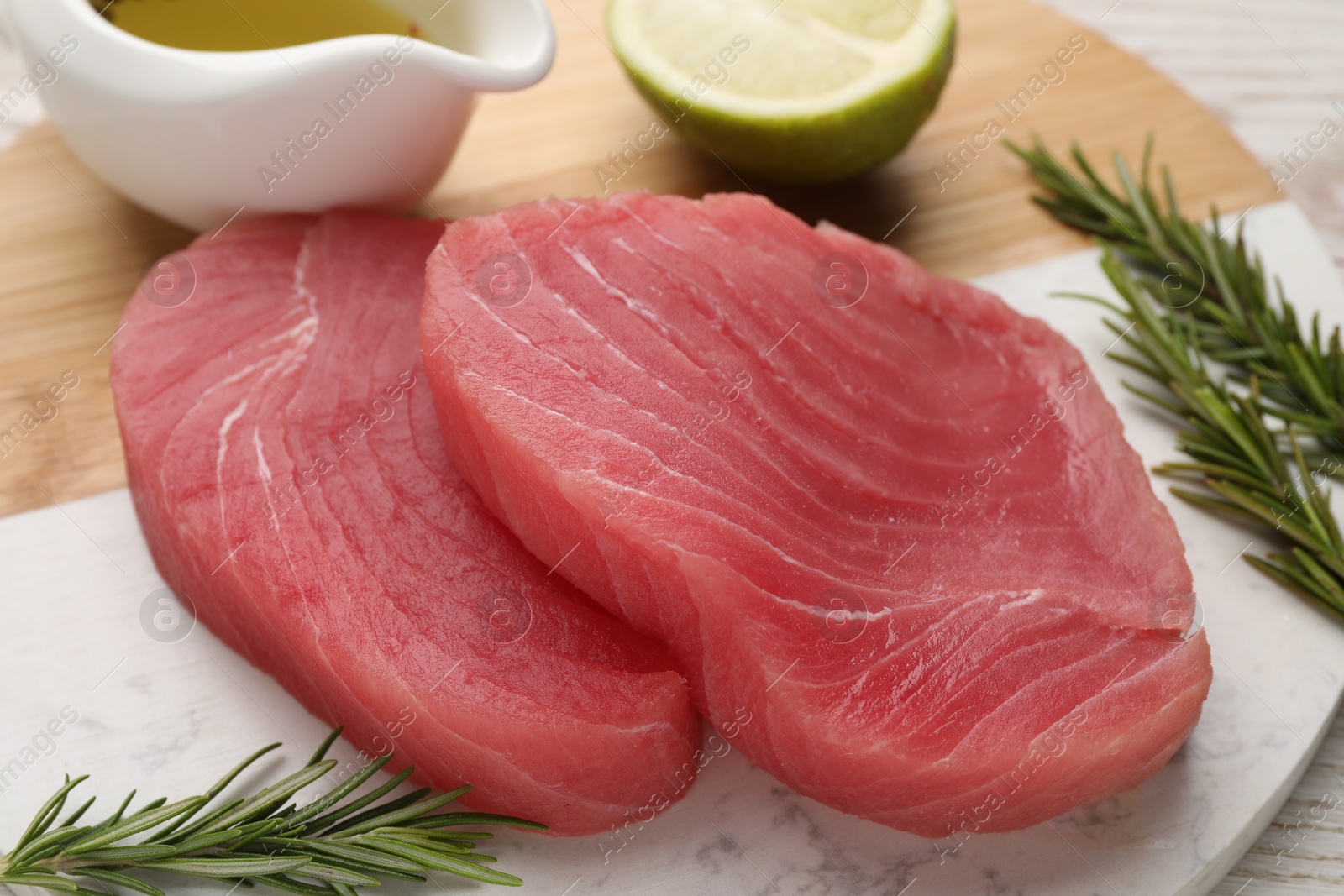 Photo of Fresh raw tuna fillets with rosemary, lime and oil on board, closeup