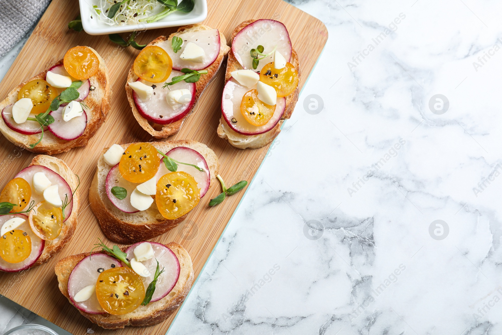 Photo of Tasty bruschettas with radish and yellow cherry tomatoes on white marble table, top view. Space for text