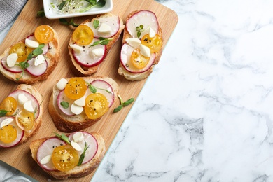 Tasty bruschettas with radish and yellow cherry tomatoes on white marble table, top view. Space for text