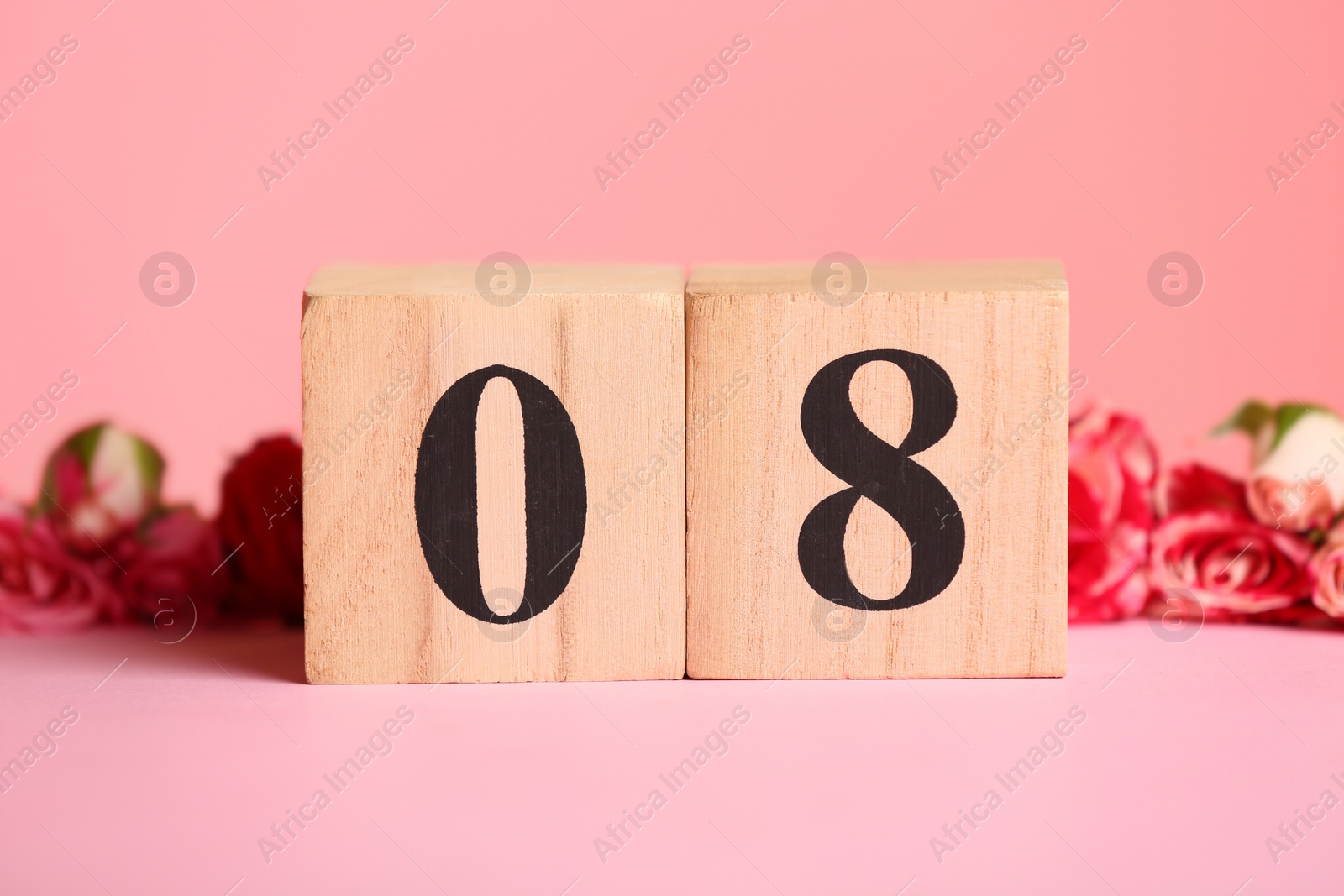 Photo of Wooden block calendar and flowers on table against color background. International Women's Day