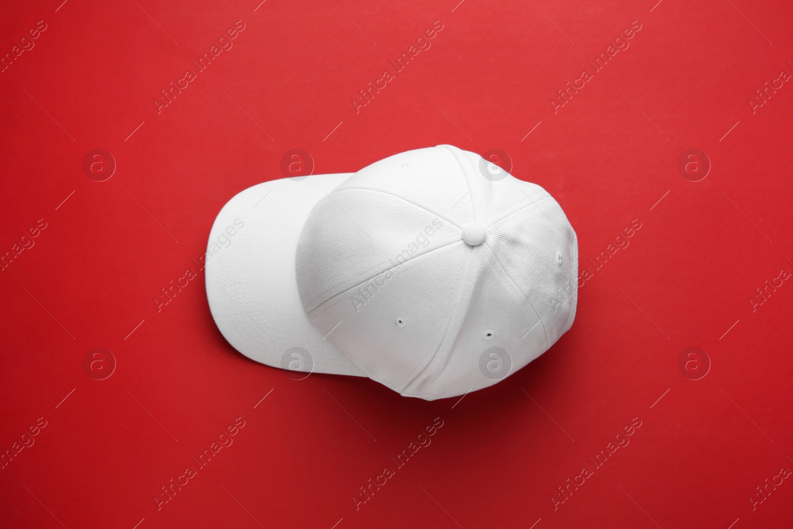 Photo of Stylish white baseball cap on red background, top view