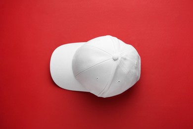 Stylish white baseball cap on red background, top view