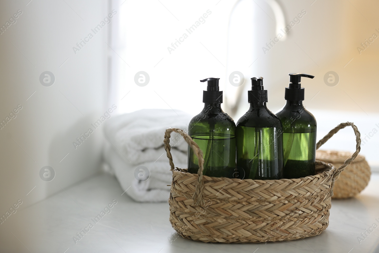 Photo of Wicker basket with soap dispensers and towels on table. Space for text