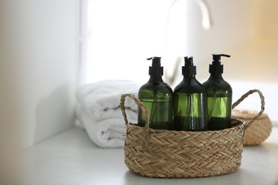 Wicker basket with soap dispensers and towels on table. Space for text