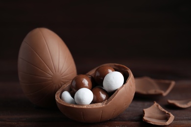 Photo of Whole and broken chocolate eggs with candies on wooden table