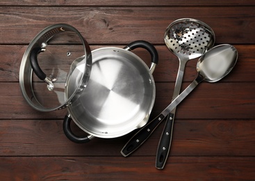 Photo of Modern saucepan, skimmer and spoon on brown wooden table. Cooking utensils