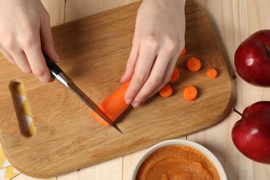 Photo of Woman cutting boiled carrot at wooden table, top view. Preparing baby food