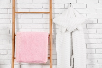 Photo of Decorative ladder with clean towel and robe near brick wall