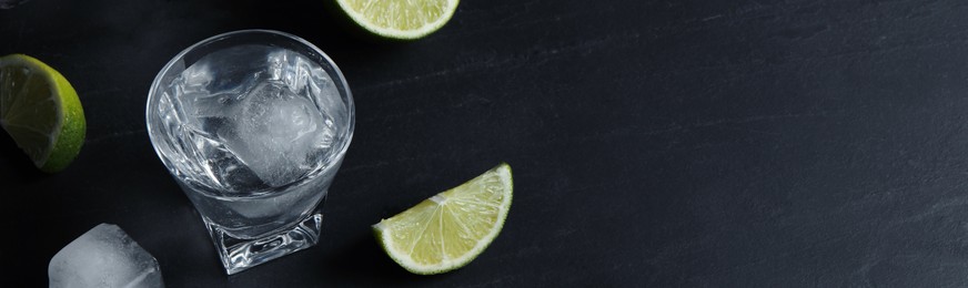 Shot glasses of vodka with lime slices and ice on black table. Space for text. Banner design