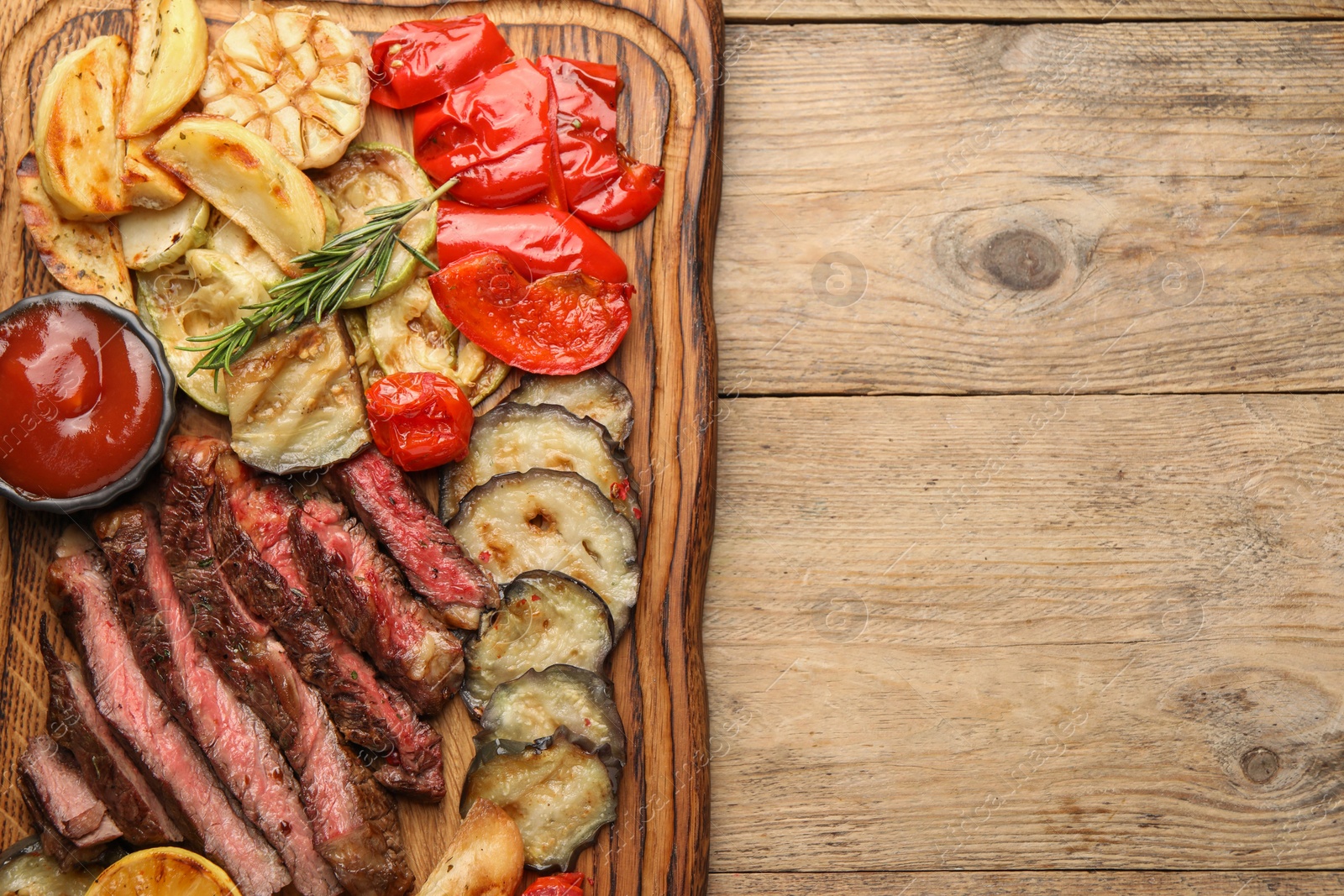 Photo of Delicious grilled beef with vegetables, spices and tomato sauce on wooden table, top view. Space for text