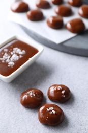 Photo of Tasty candies, caramel sauce and salt on light grey table