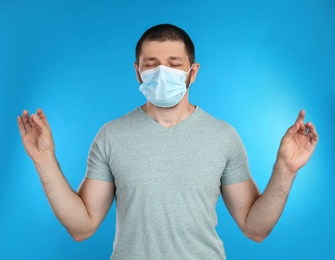Photo of Man in protective mask meditating on light blue background. Dealing with stress caused by COVID‑19 pandemic