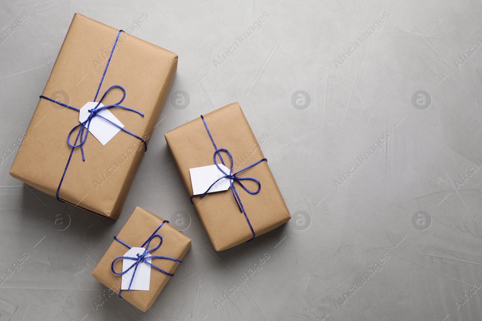 Photo of Parcels wrapped in kraft paper with tags on light grey table, flat lay. Space for text