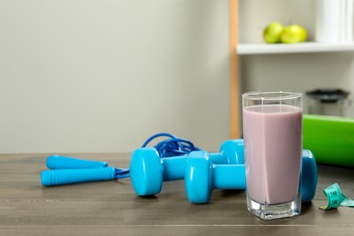 Photo of Tasty shake and sports equipment on wooden table indoors, space for text. Weight loss