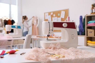 Photo of Dressmaker working in atelier, focus on table with sewing machine and accessories