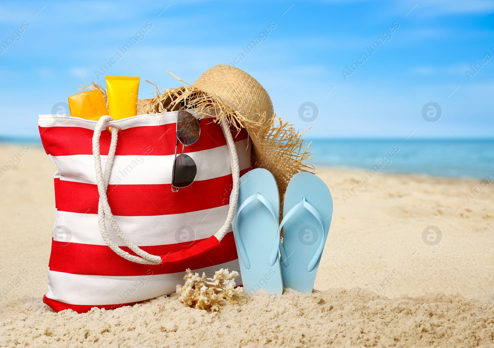 Image of Stylish bag with different accessories on sandy beach near ocean