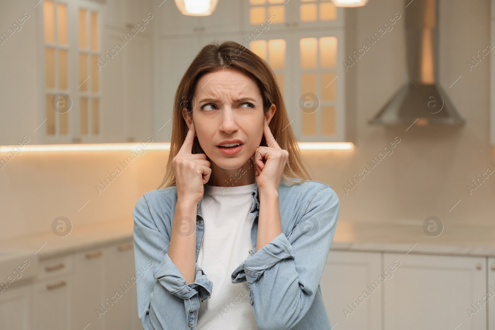 Photo of Emotional young woman covering her ears with fingers at home