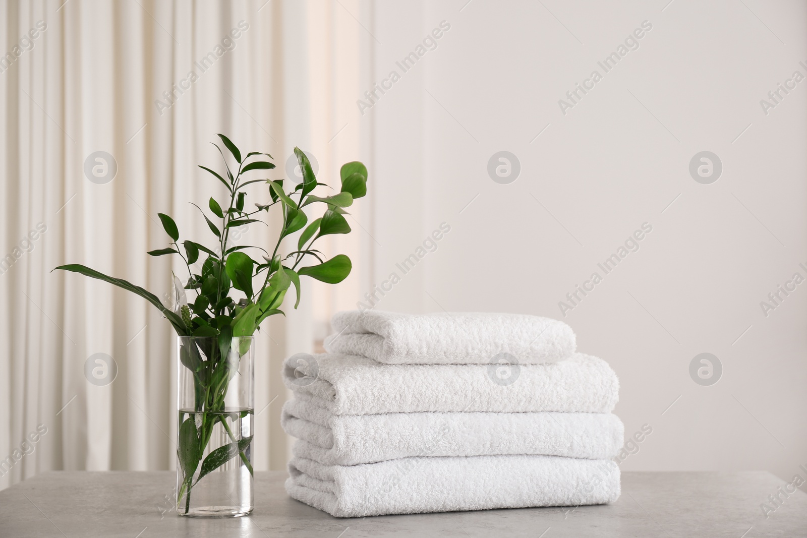 Photo of Fresh towels and green branches on light grey stone table in bathroom