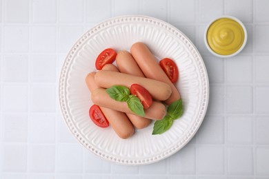 Photo of Delicious boiled sausages with tomatoes, basil and sauce on white tiled table, top view