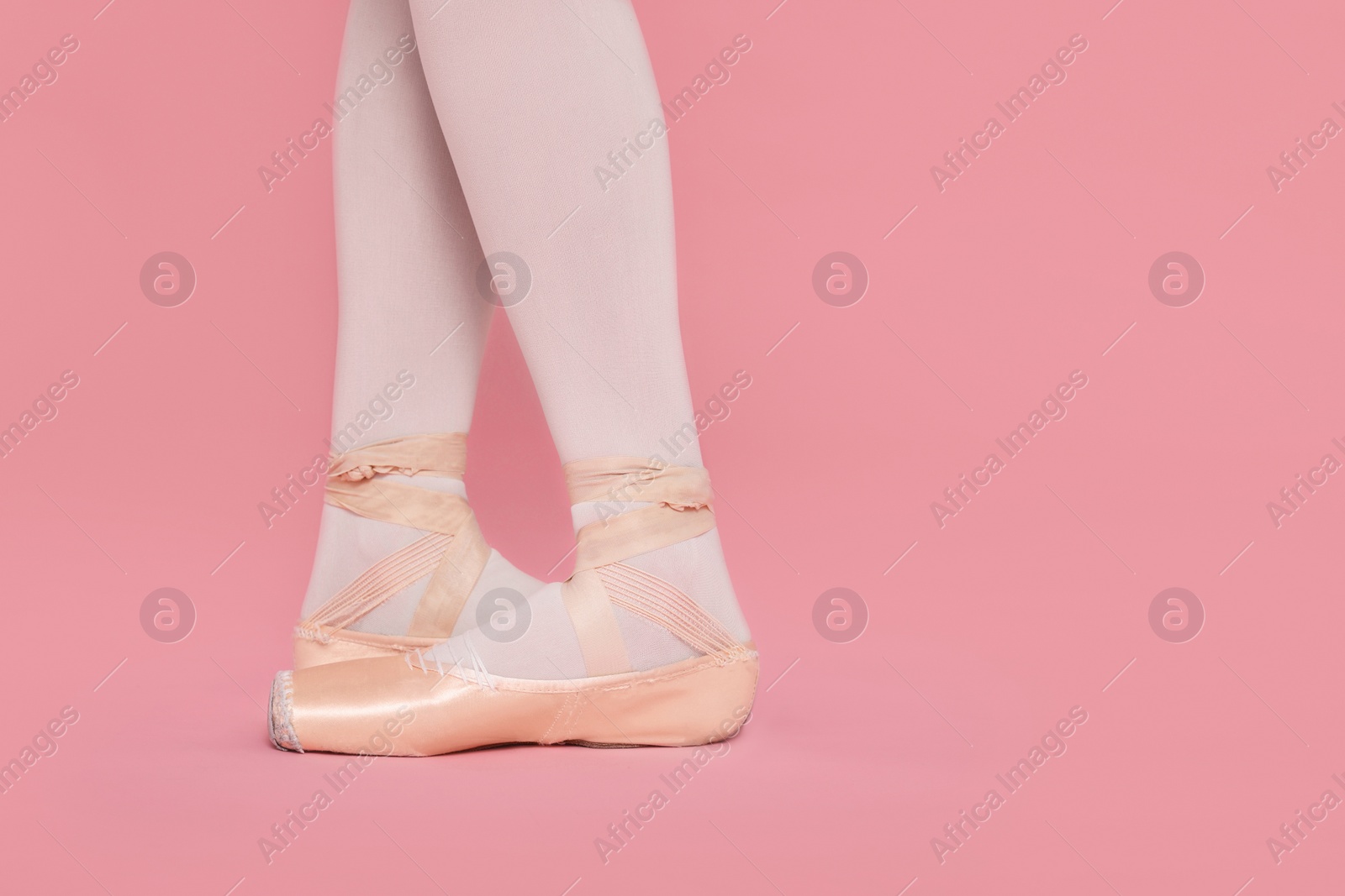 Photo of Young ballerina in pointe shoes practicing dance moves on pink background, closeup. Space for text