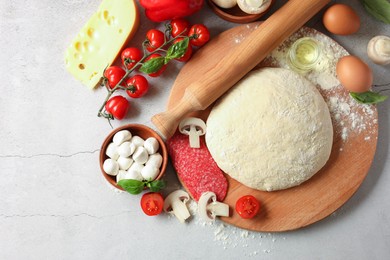 Pizza dough, products and rolling pin on gray textured table, flat lay