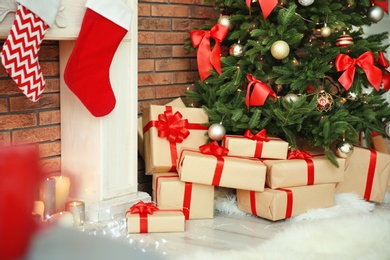 Photo of Beautiful Christmas tree and gifts near decorative fireplace with stockings indoors