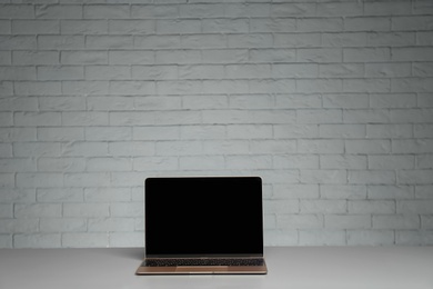 Photo of Modern laptop with blank screen on table against brick wall