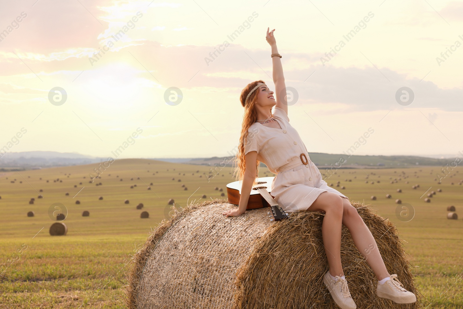 Photo of Beautiful hippie woman with guitar on hay bale in field, space for text