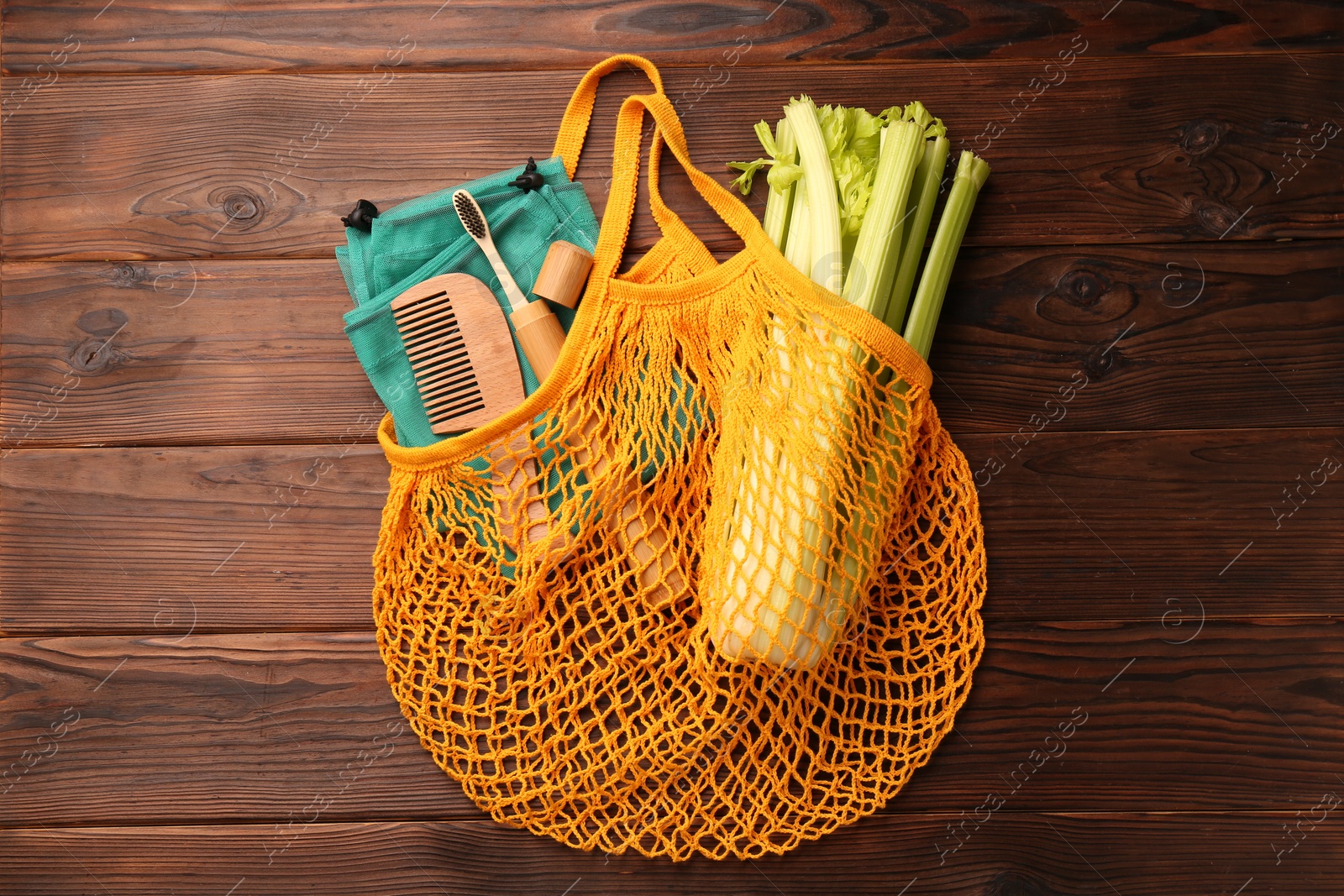 Photo of Fishnet bag with different items on wooden table, top view. Conscious consumption