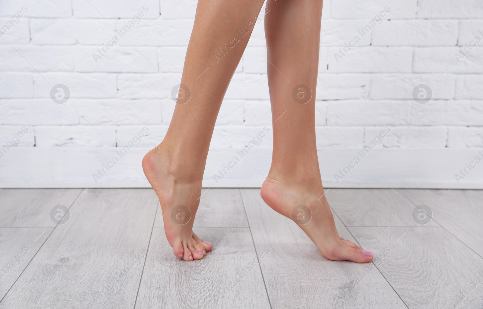 Photo of Woman with beautiful legs and feet near brick wall indoors, closeup. Spa treatment