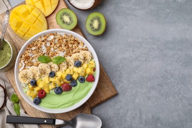 Tasty matcha smoothie bowl with fresh fruits and oatmeal served on grey table, flat lay with space for text. Healthy breakfast