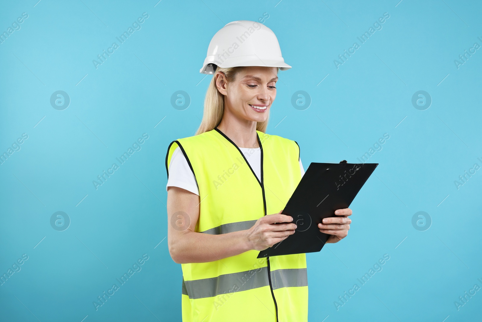 Photo of Engineer in hard hat holding clipboard on light blue background