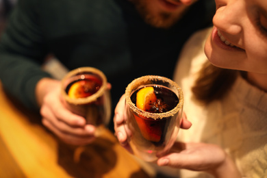 Photo of Lovely couple with tasty mulled wine at table in cafe, closeup