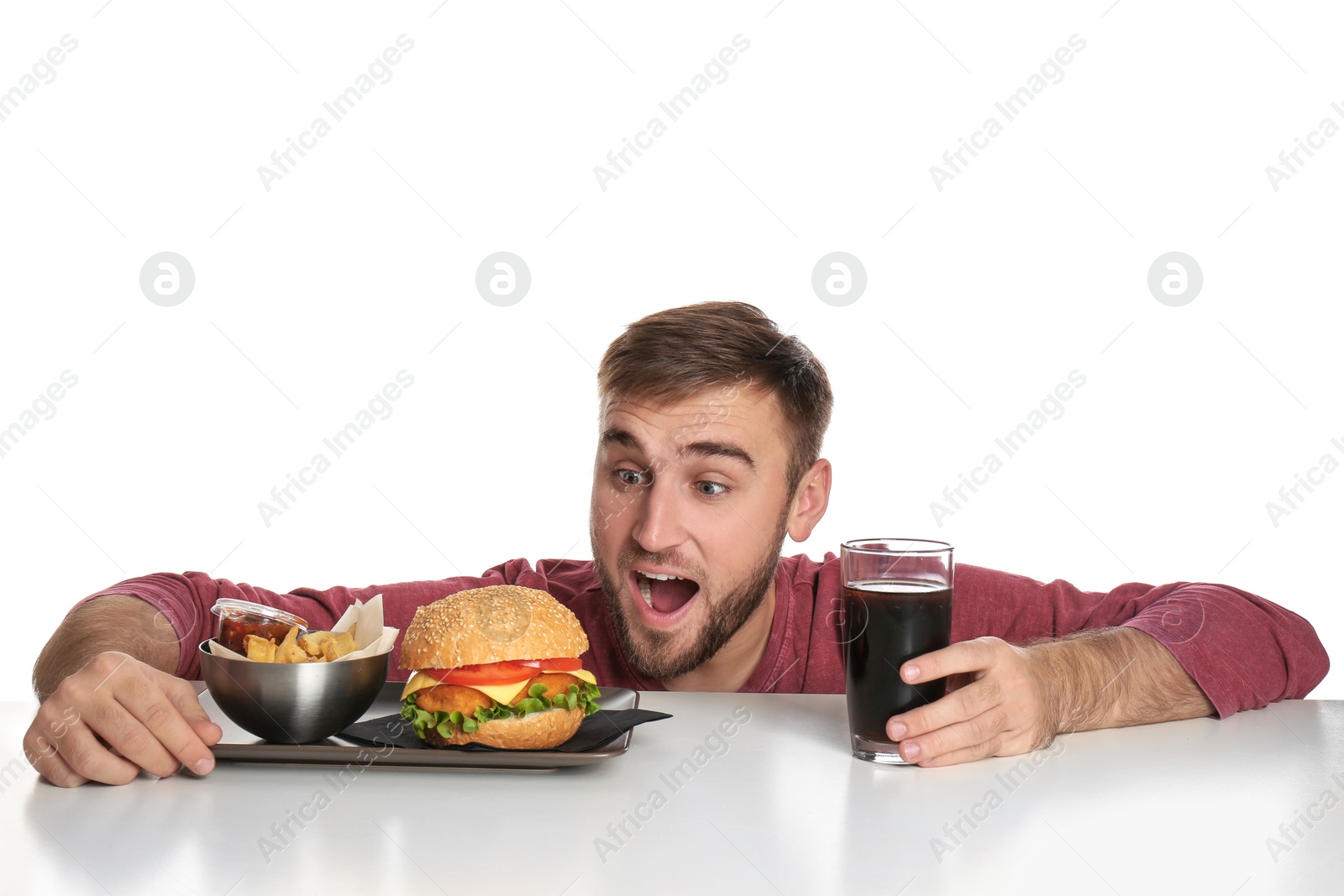 Photo of Young hungry man with glass of cola, tasty burger and French fries on white background
