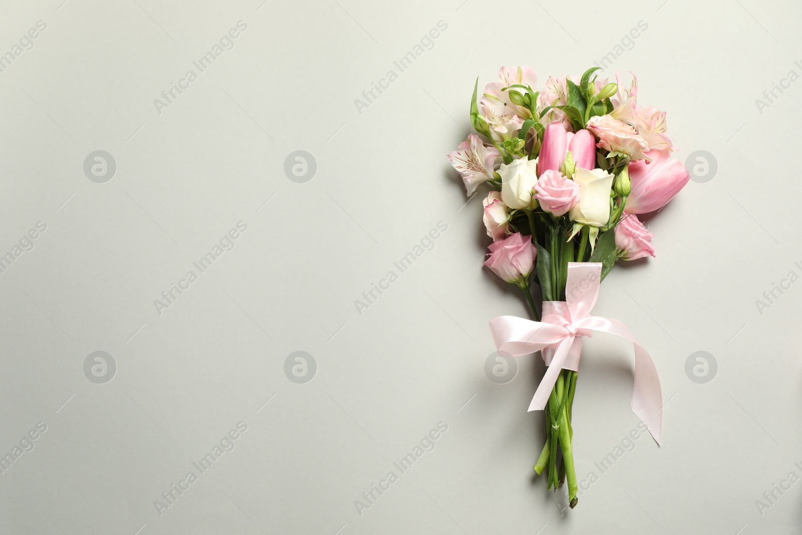 Photo of Happy Mother's Day. Bouquet of beautiful flowers tied with pink ribbon on light grey background, top view. Space for text