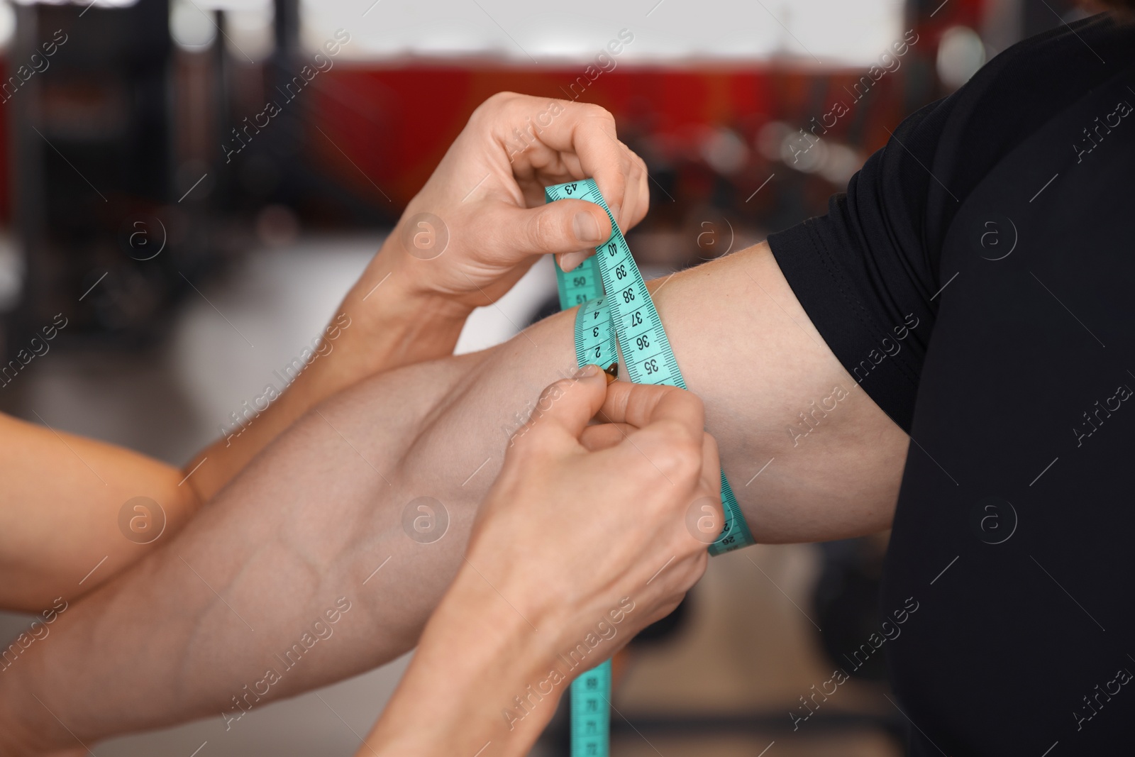 Photo of Trainer measuring man`s biceps with tape in gym, closeup