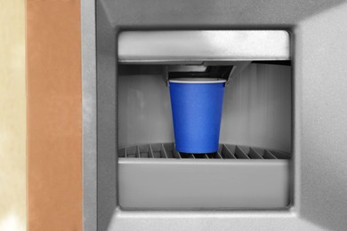 Photo of Blue paper cup with coffee in vending machine
