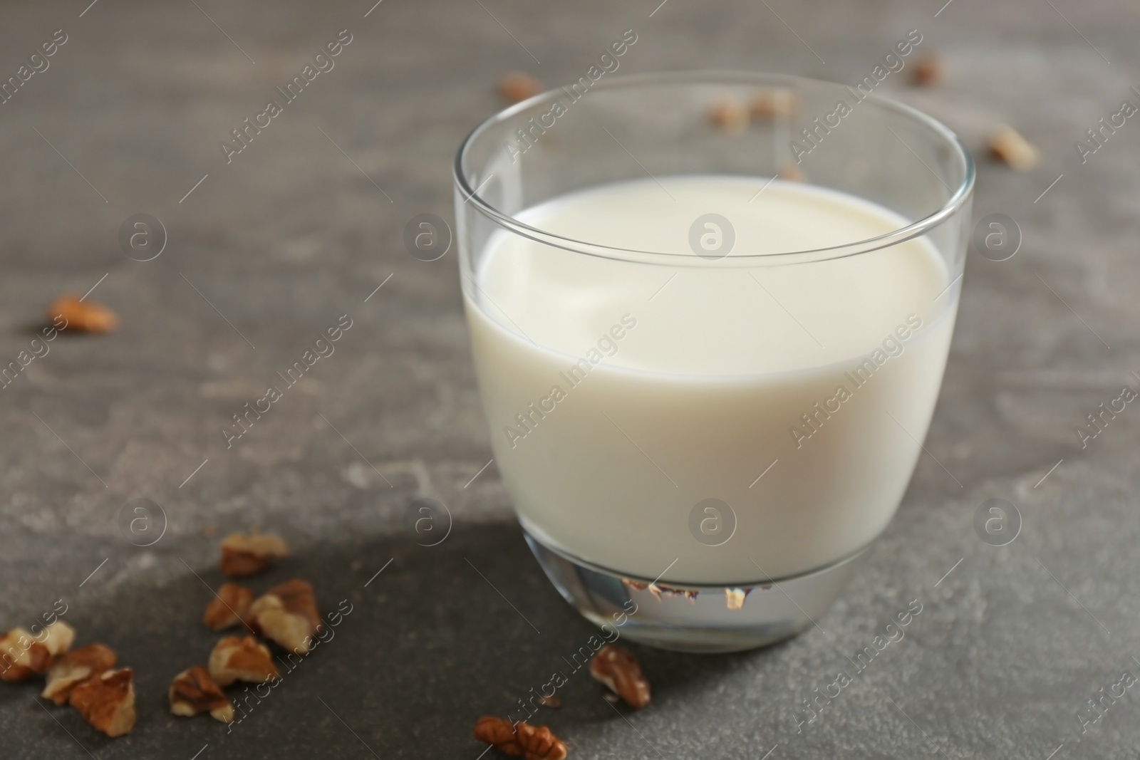 Photo of Glass with milk and nuts on grey background