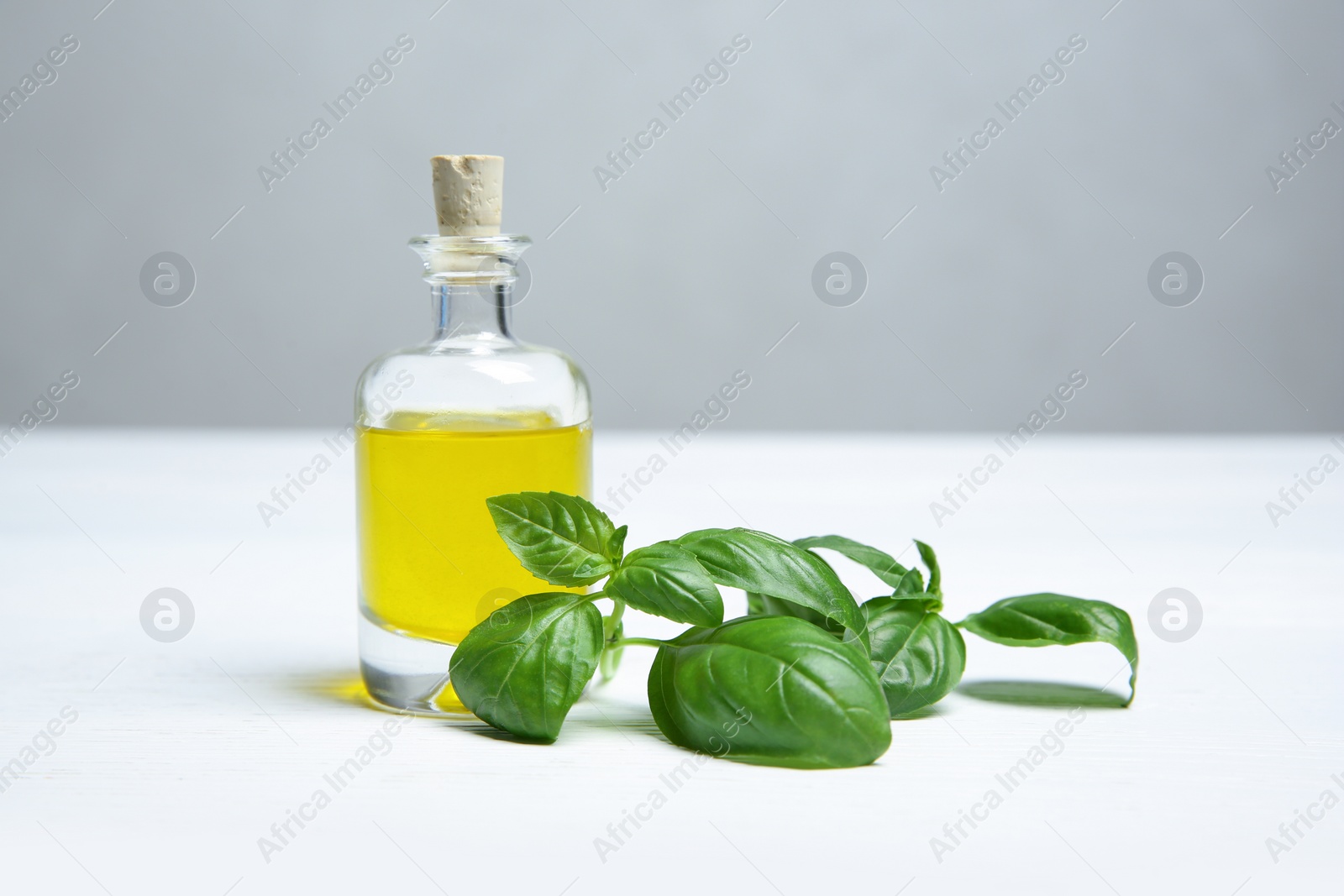 Photo of Glass bottle of oil and basil leaves on light table. Space for text