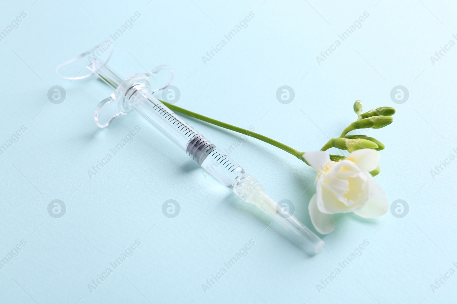 Photo of Cosmetology. Medical syringe and freesia flower on light blue background, closeup