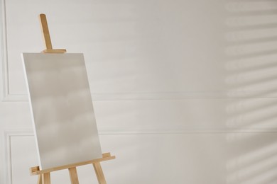 Wooden easel with blank canvas on light background. Space for text